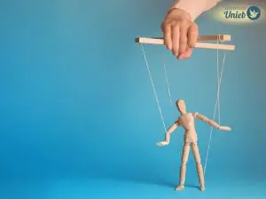 Pequeno boneco de madeira do tipo marionete preso por cordas a uma base de madeira que é segurada por uma mão no alto