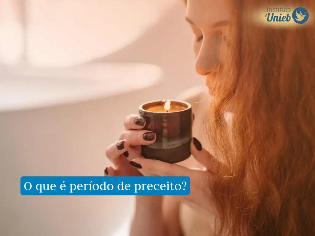 Mulher com cabelos soltos cobrindo parte do rosto segurando com as duas mãos um pote escuro com uma vela acesa