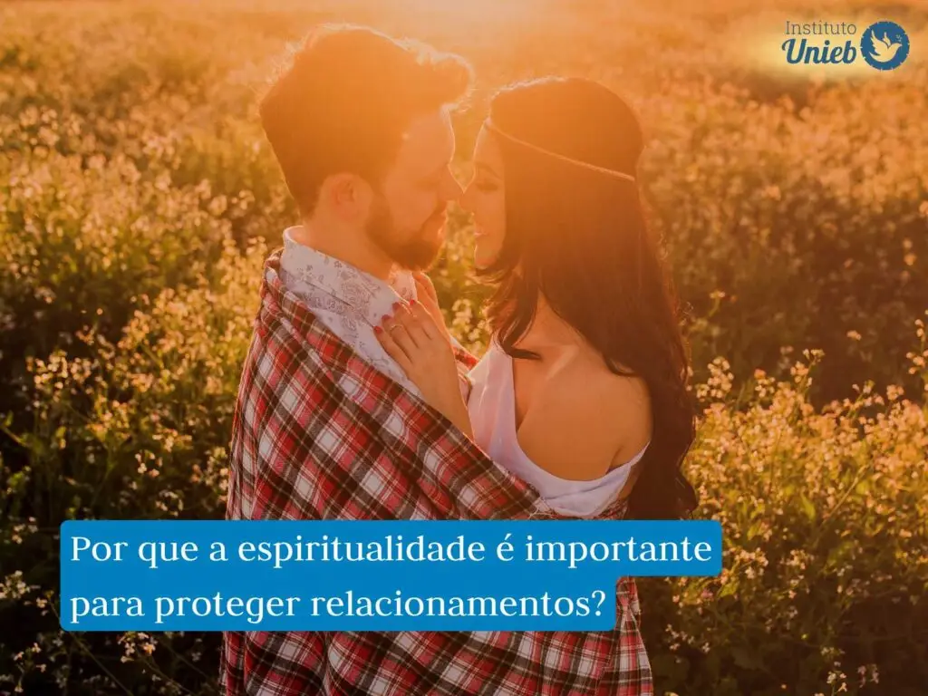 Casal de homem e mulher abraçados olhando de nos olhos um do outro em um local aberto com flores no terreno e raios de sol indicando um entardecer