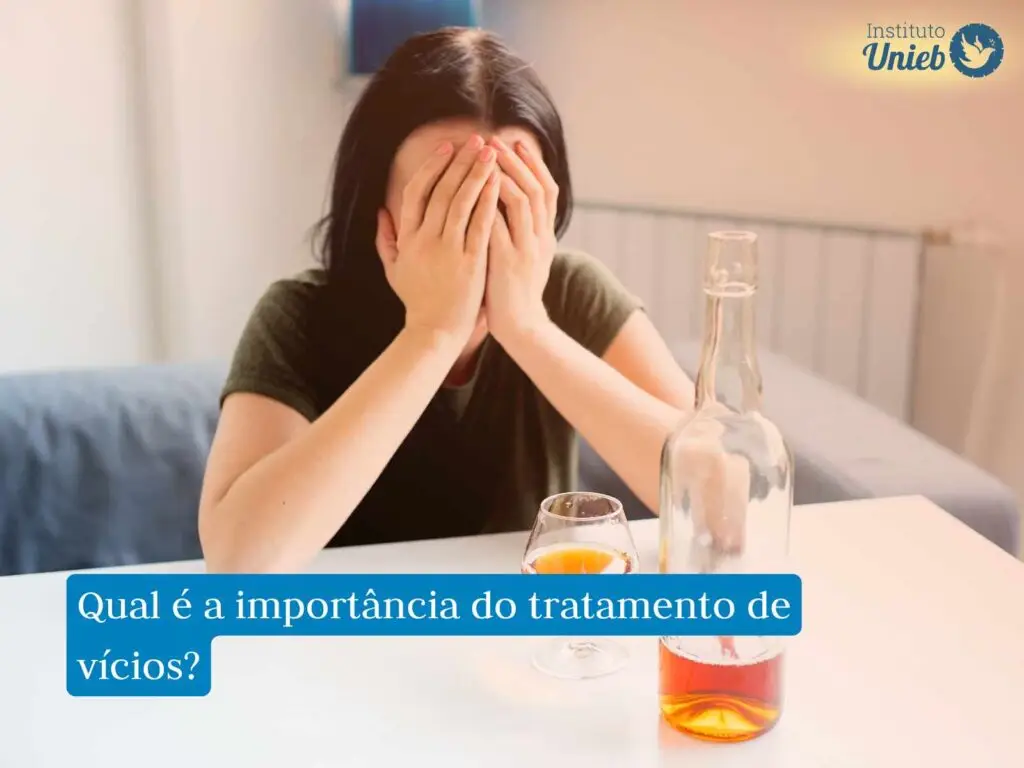 Pessoa com roupa preta sentada à mesa com mão no rosto e garrafa e copo com bebida na cor dourada