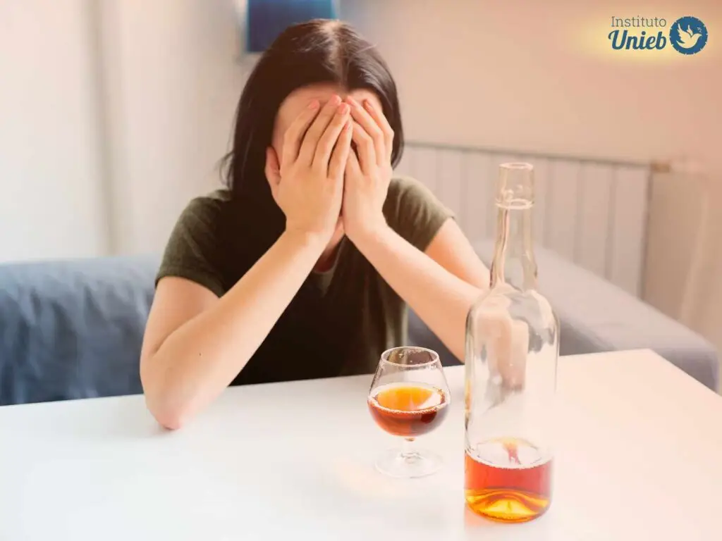 Pessoa com roupa preta sentada à mesa com mão no rosto e garrafa e copo com bebida na cor dourada - Instituto Unieb (Pai de santo Roberson Dariel) - Contato 11 96982-1121 - CEP 14801-040 - Av. Dom Pedro II 562, Centro, Araraquara, SP