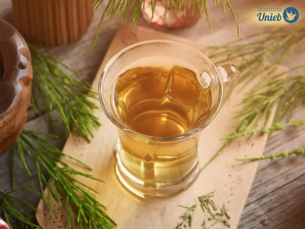 Jarra de vidro com líquido amarelo em cima de uma base de madeira com ervas espalhadas pela mesa - Instituto Unieb (Pai de santo Roberson Dariel) - Contato 11 96982-1121 - CEP 14801-040 - Av. Dom Pedro II 562, Centro, Araraquara, SP