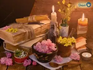 Elementos ritualísticos sob a mesa, como flores em tons de rosa, vela acesa, livro amarrado e fechado - Instituto Unieb (Pai de santo Roberson Dariel) - Contato 11 96982-1121 - CEP 14801-040 - Av. Dom Pedro II 562, Centro, Araraquara, SP