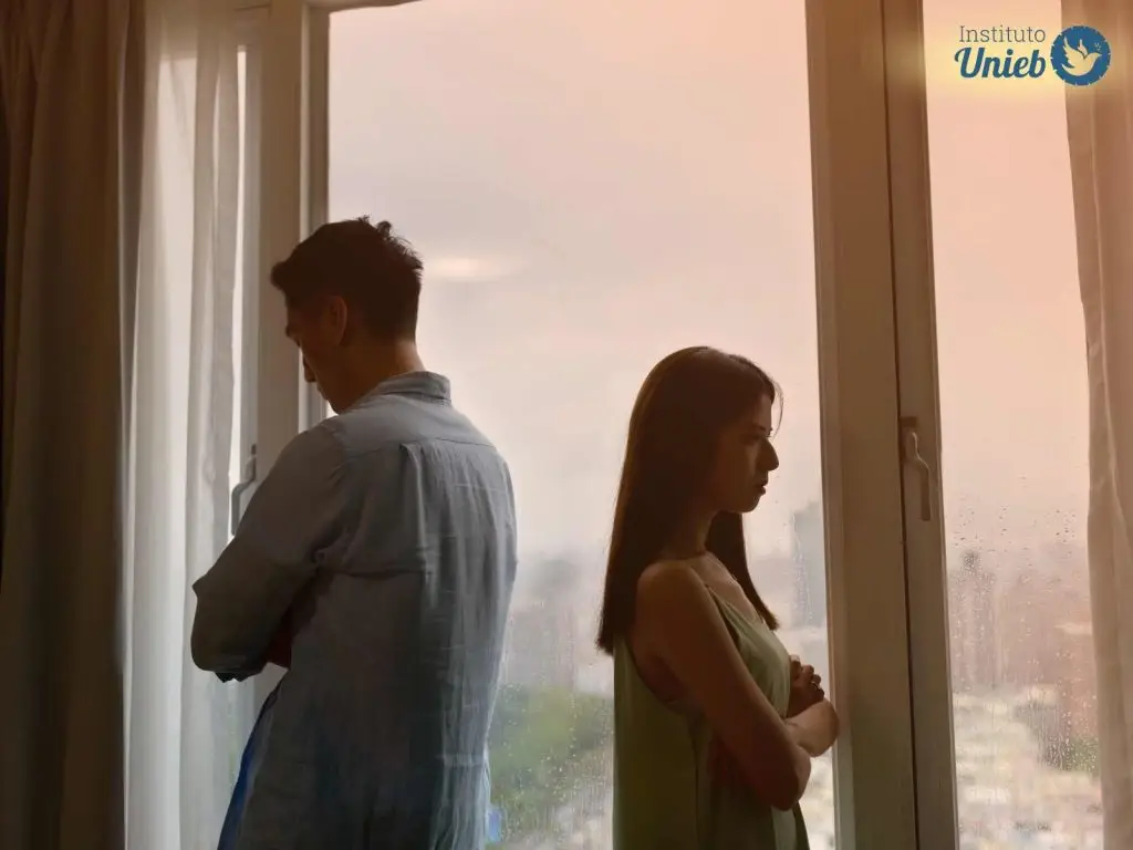 Homem e mulher virados de costas um para o outro próximo a uma janela