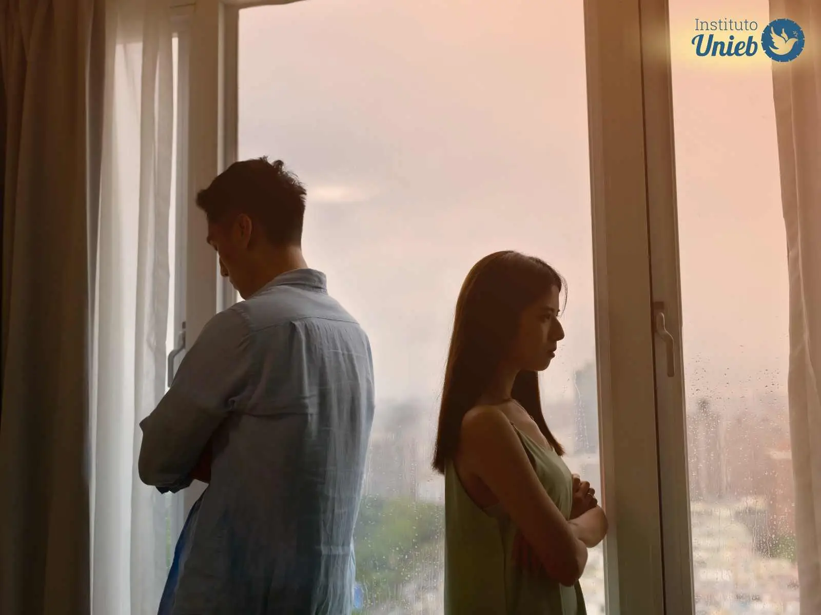 Homem e mulher virados de costas um para o outro próximo a uma janela