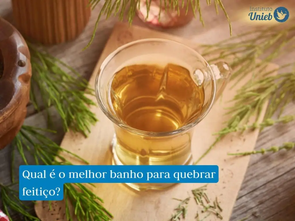 Jarra de vidro com líquido amarelo em cima de uma base de madeira com ervas espalhadas pela mesa