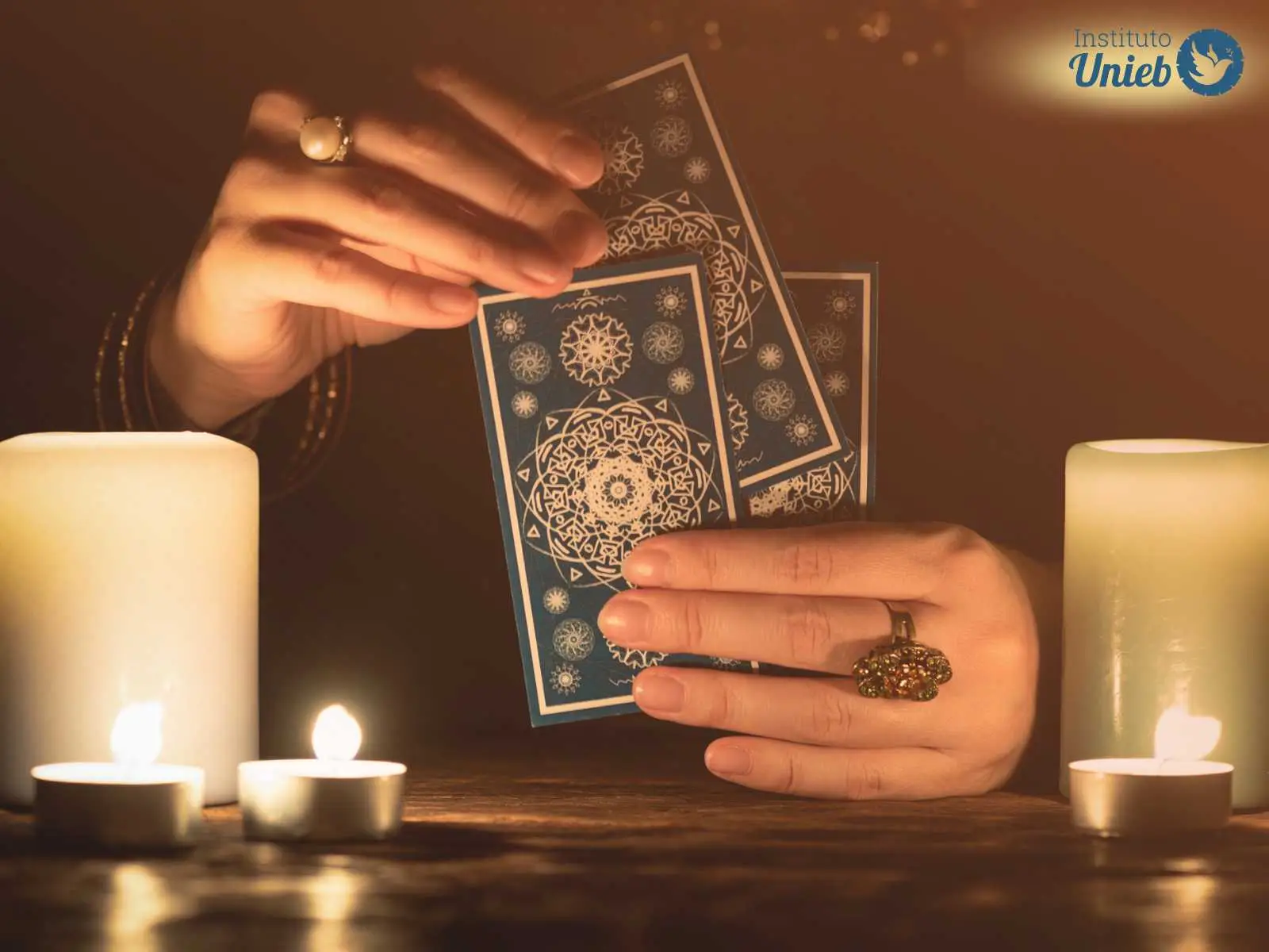 Mãos femininas segurando cartas de Tarot próximo a uma mesa de madeira onde há velas acesas - Instituto Unieb (Pai de santo Roberson Dariel) - Contato 11 96982-1121 - CEP 14801-040 - Av. Dom Pedro II 562, Centro, Araraquara, SP