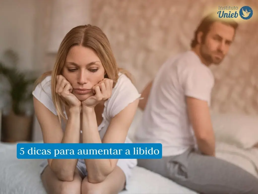 Homem e mulher sentados na cama vestindo camiseta branca com expressão de tristeza