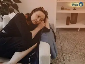 Mulher de meia-idade deitada no sofá com a cabeça apoiada nos braços com expressão triste no rosto