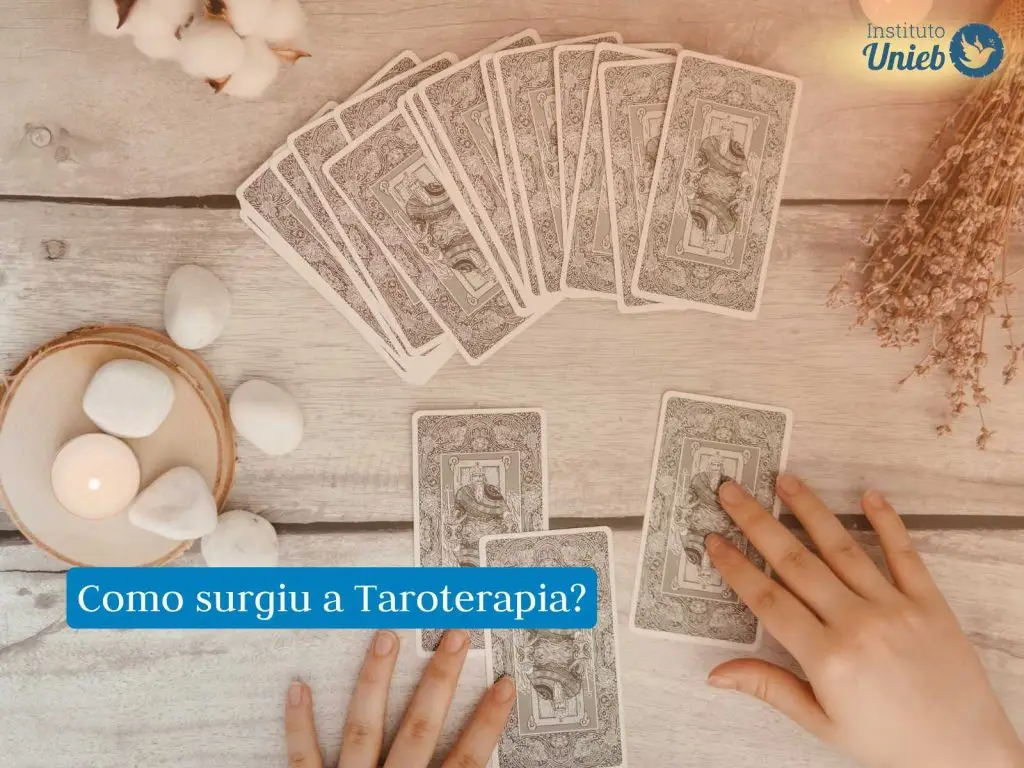 Mesa com cartas de Tarot enfileiradas, pedras e cristais energéticos do lado esquerdo e as mãos de uma pessoa escolhendo cartas