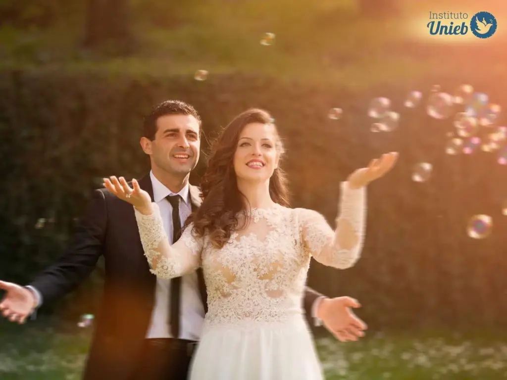 Homem vestido de terno preto e mulher com vestido de noiva em um ambiente aberto sorrindo com bolas de sabão no ar - Instituto Unieb (Pai de santo Roberson Dariel) - Contato 11 96982-1121 - CEP 14801-040 - Av. Dom Pedro II 562, Centro, Araraquara, SP