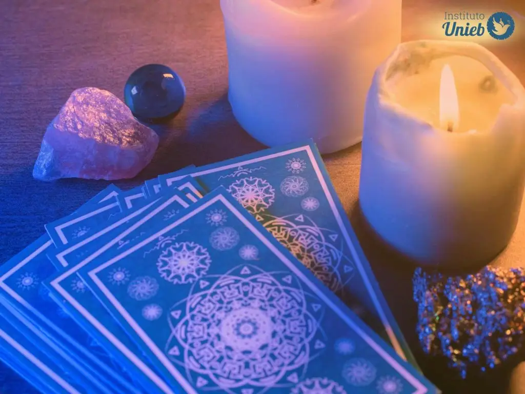 Cartas de Tarot sob a mesa de madeira ao lado de duas velas acesas e cristais energéticos - Instituto Unieb (Pai de santo Roberson Dariel) - Contato 11 96982-1121 - CEP 14801-040 - Av. Dom Pedro II 562, Centro, Araraquara, SP
