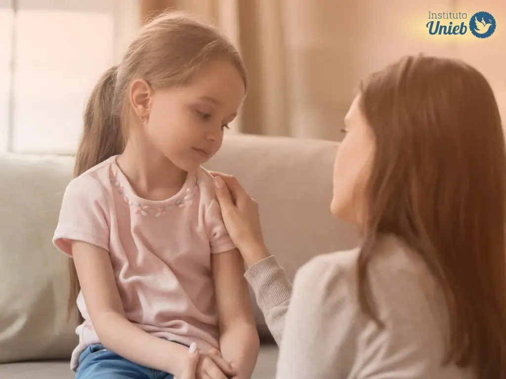 Mulher de costas para câmera consolando menina sentada no sofá de frente
