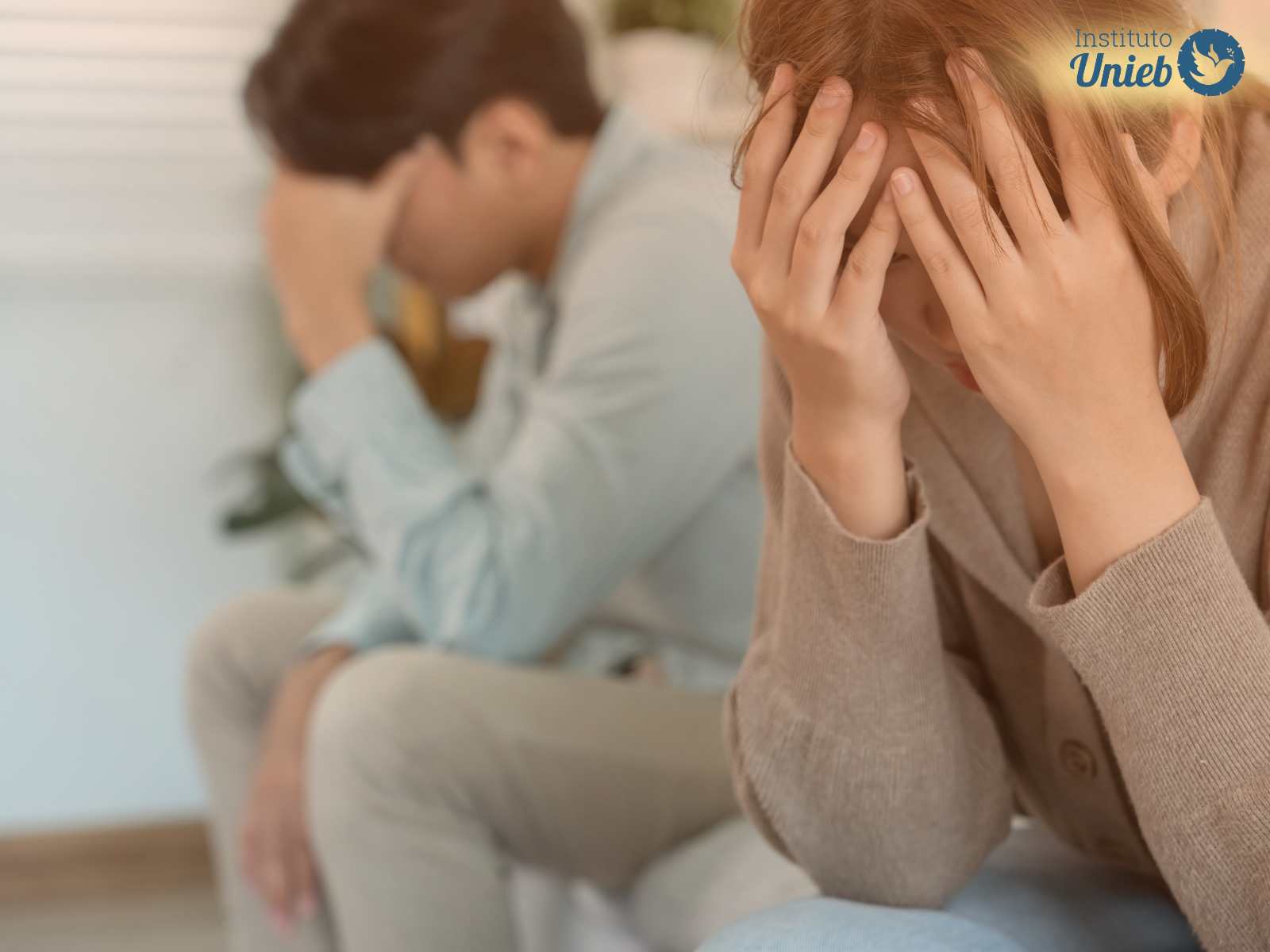 Homem e mulher sentados cada um com a cabeça apoiada nas mãos