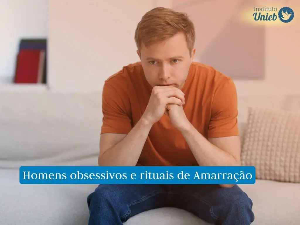 Homem vestindo camiseta laranja sentado no sofá com mãos fechadas e queixo apoiado