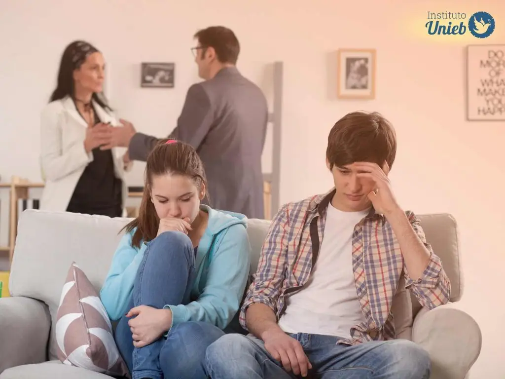 Casal de homem e mulher brigando ao fundo e casal de filhos adolescentes sentados no sofá com preocupação, indicando um momento de conflito amoroso com a presença dos filhos