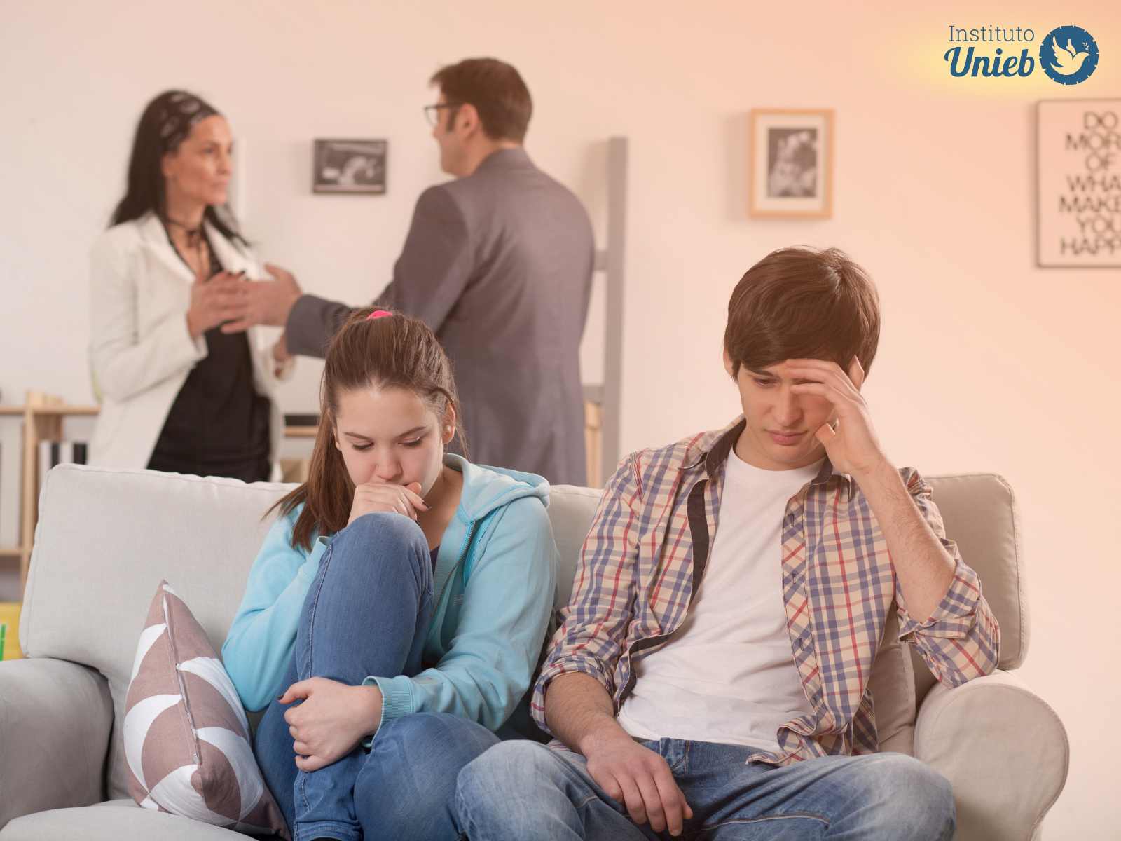 Casal de homem e mulher brigando ao fundo e casal de filhos adolescentes sentados no sofá com preocupação
