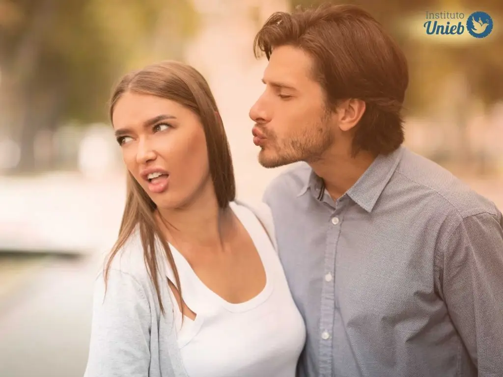 Homem tentando beijar mulher enquanto ela vira o rosto e faz uma expressão de nojo, indicando uma parceira que sente desprezo ao ser tocada pelo parceiro