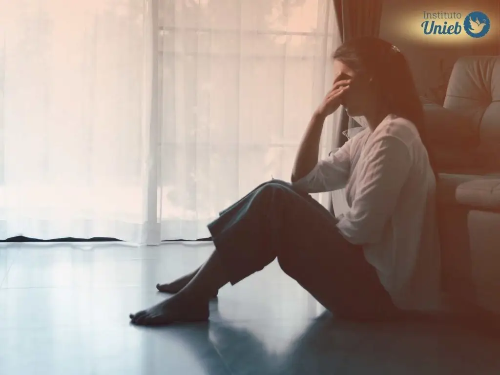 Mulher sentada no chão com a mão no rosto indicando em estado de perturbação mental, como quando alguém passa por obsessão espiritual