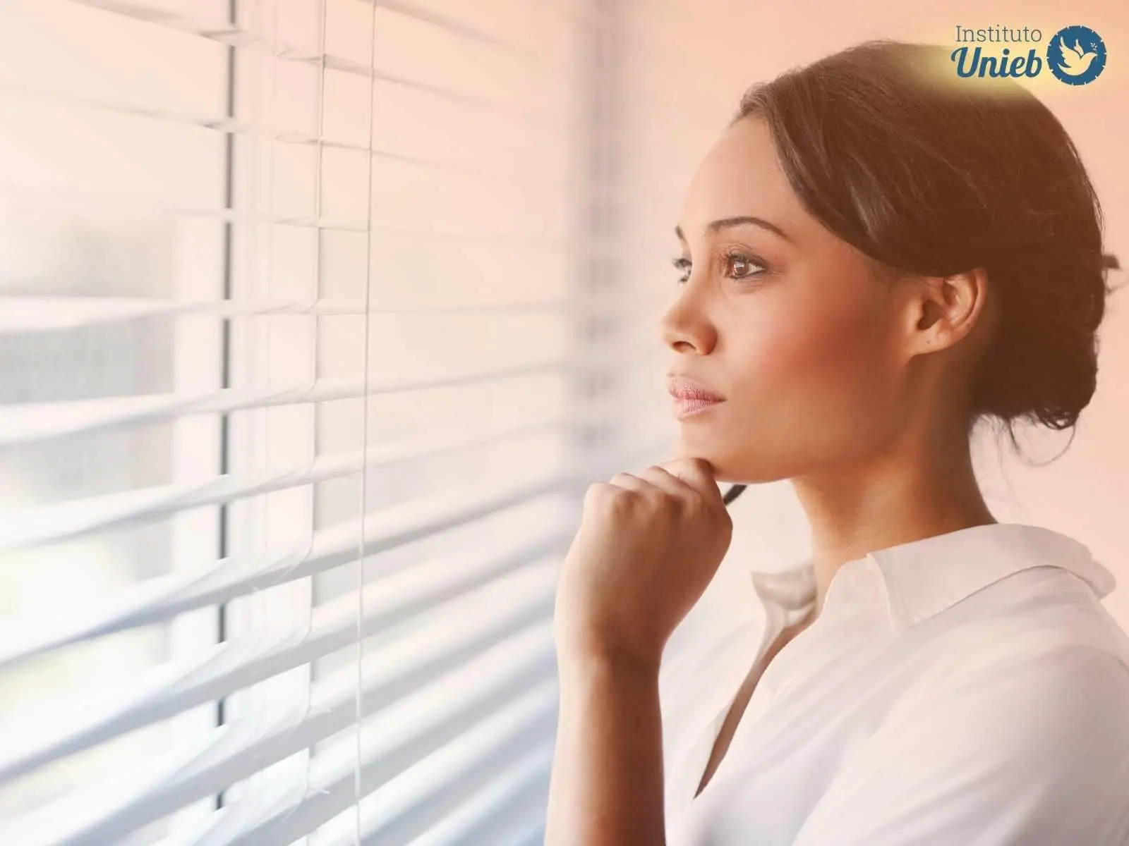 Mulher olhando pela janela com expressão pensativa, ilustrando uma pessoa sob efeito do Trabalho de Vira Pensamento