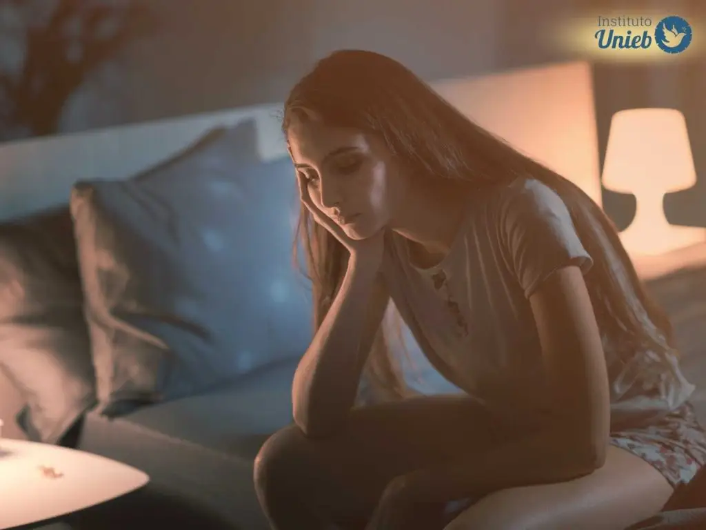 Mulher sentada sozinha na cama vestindo pijama indicando um casal que está dormindo em quartos separados