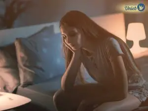 Mulher sentada sozinha na cama vestindo pijama indicando um casal que está dormindo em quartos separados