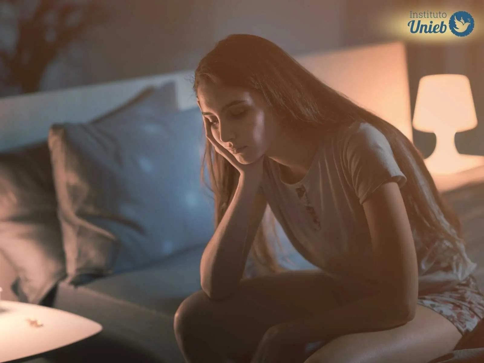 Mulher sentada sozinha na cama vestindo pijama indicando um casal que está dormindo em quartos separados