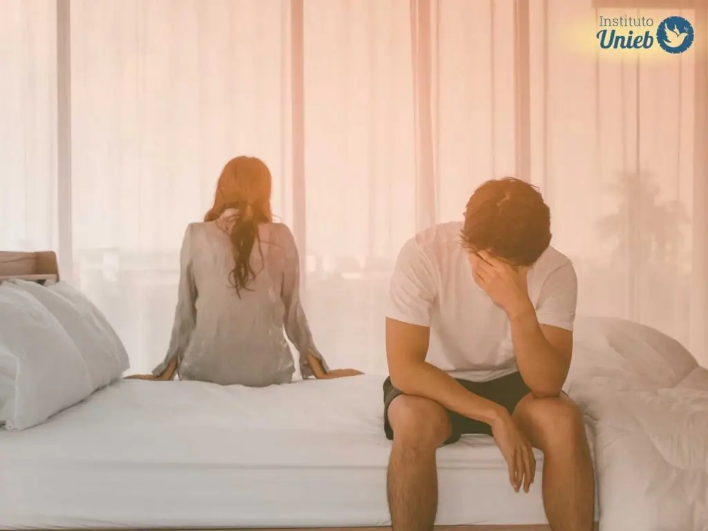 Homem e mulher sentados na cama distantes, representando um marido distante no relacionamento