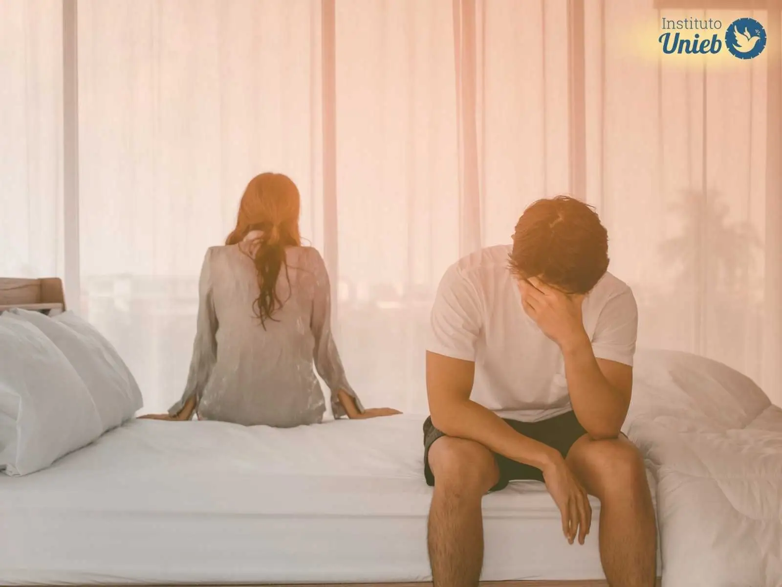 Homem e mulher sentados na cama distantes, representando um marido distante no relacionamento