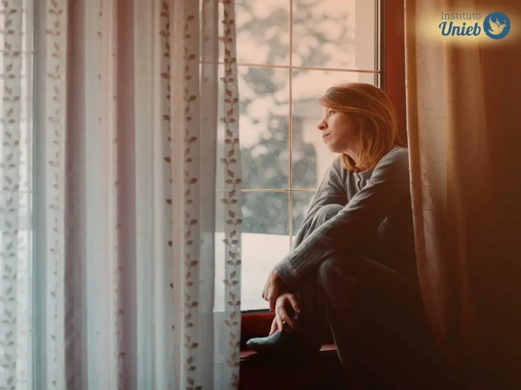 Mulher olhando pela janela representando uma esposa que discutiu com o parceiro e olha pela janela esperando ele voltar após uma discussão