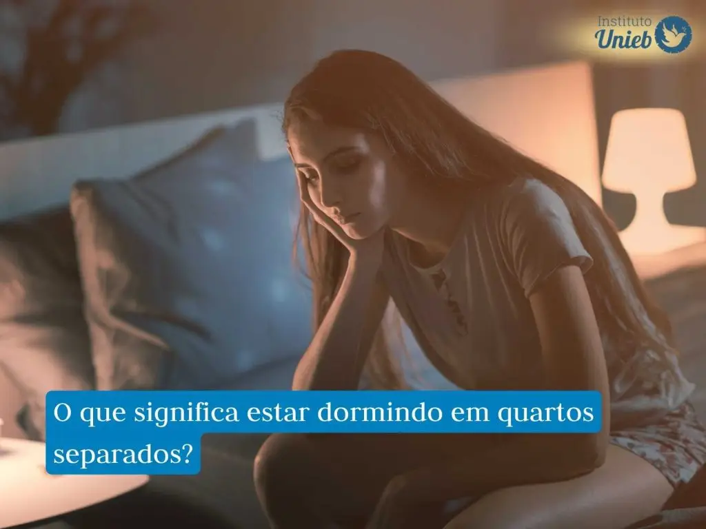 Mulher sentada sozinha na cama vestindo pijama indicando um casal que está dormindo em quartos separados