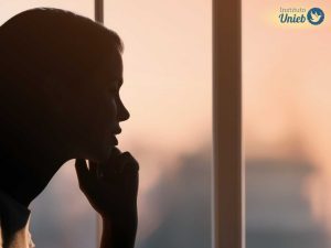 Mulher olhando pela janela representando alguém pensativo que reflete sobre amar duas pessoas ao mesmo tempo