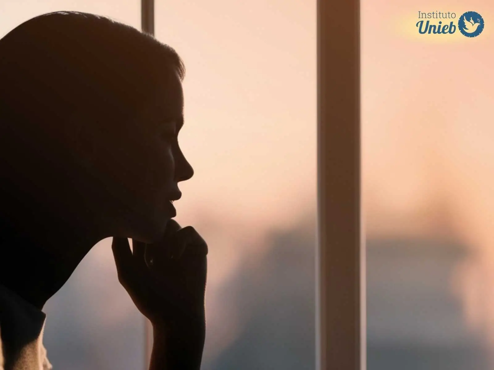 Mulher olhando pela janela representando alguém pensativo que reflete sobre amar duas pessoas ao mesmo tempo