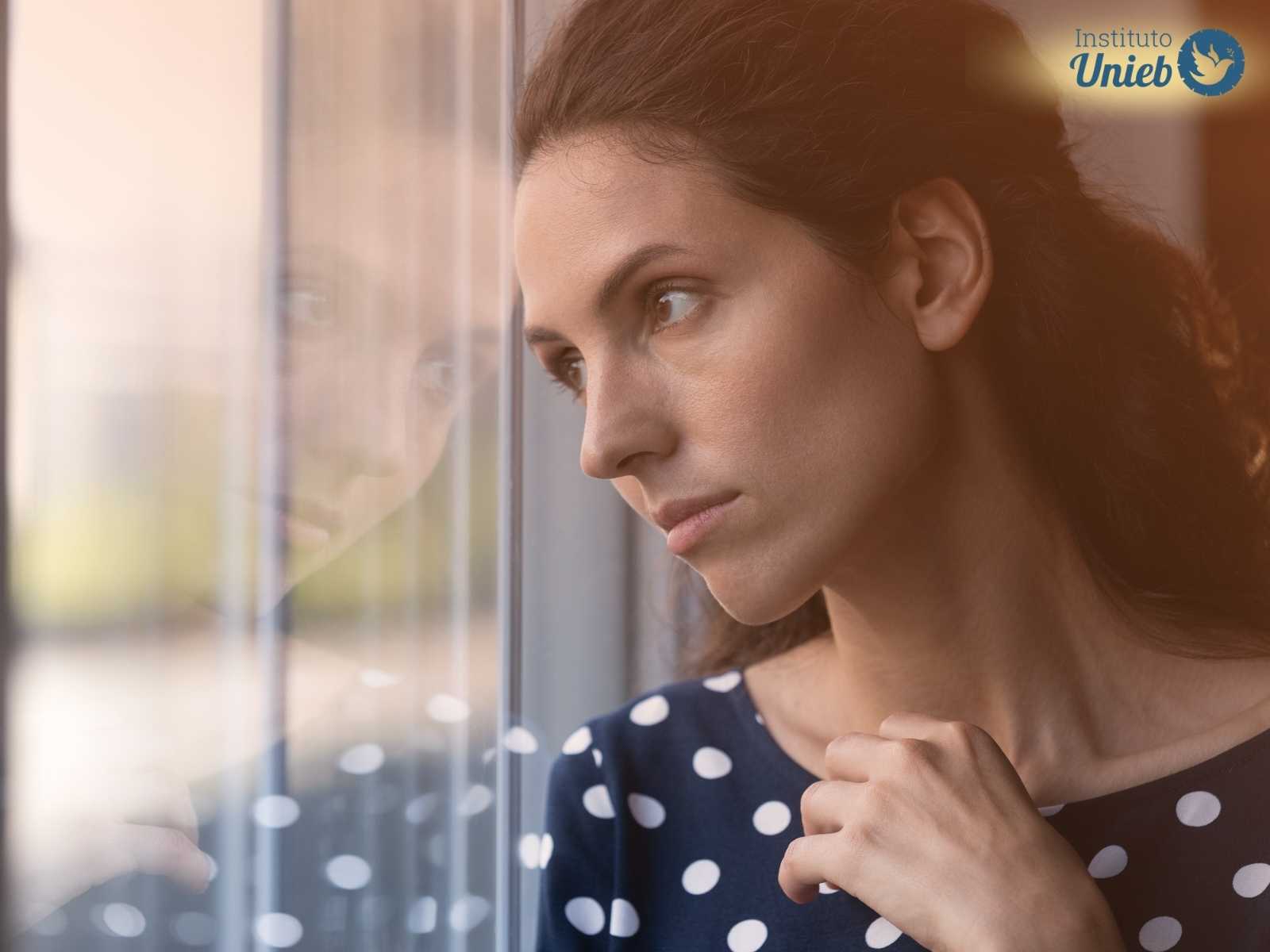 Mulher olhando pela janela pensativa como quem reflete sobre não conseguir amar quem a ama