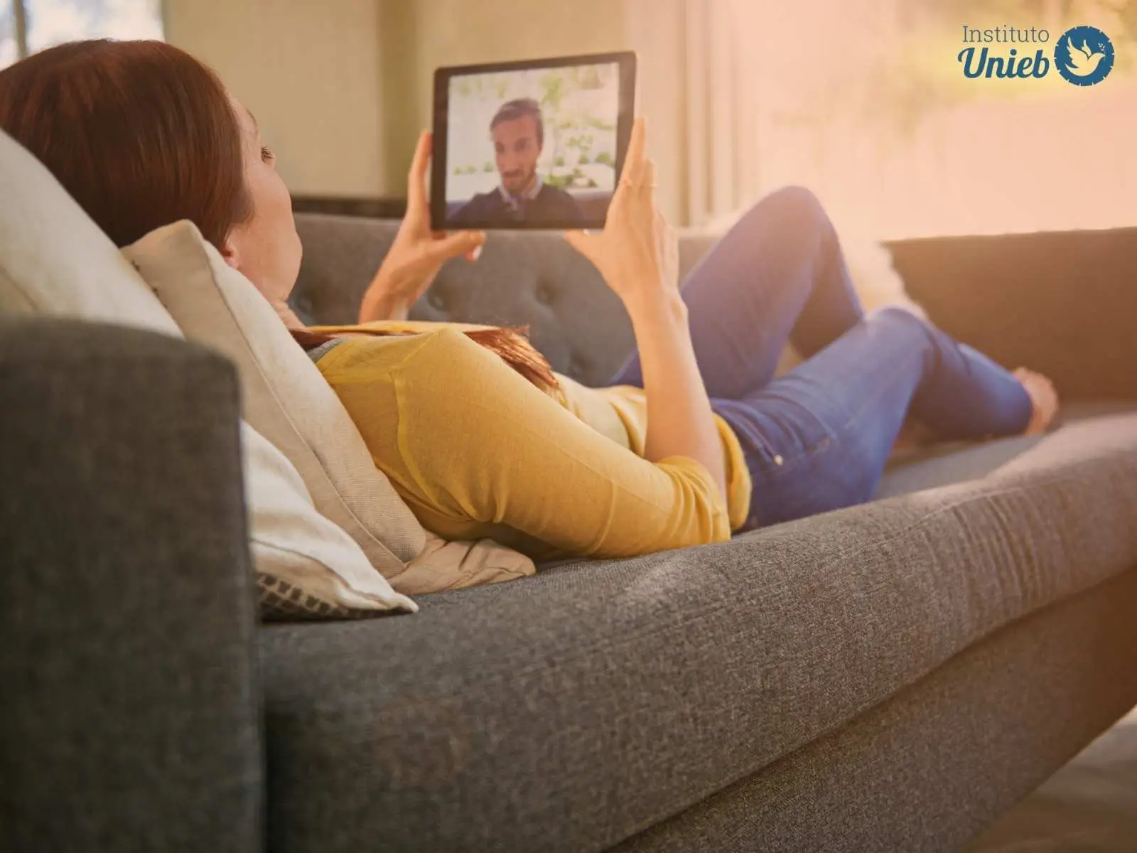 Mulher deitada no sofá com tablet conversando com parceiro representando um relacionamento à distância