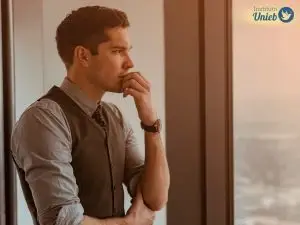 Homem pensativo olhando pela janela representando um homem que está o dia todo pensando em uma pessoa